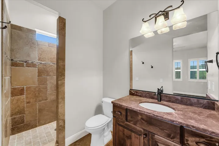 Walk-in shower with natural stone-look tile, wood-finish vanity with an integrated sink, and a sconce light fixture