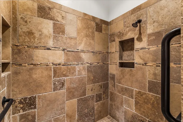 Shower with varied-size stone-look wall tiling, mosaic accent bands, a built-in shower niche, a dark bronze showerhead, and a dark bronze grab bar