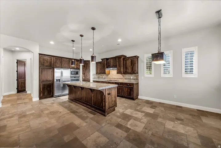 Kitchen featuring dark wood cabinetry, a center island with a stone countertop, stainless steel appliances, and pendant lighting