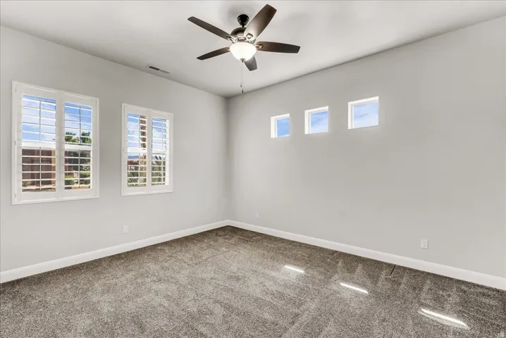 Spacious room featuring carpeting, a ceiling fan with integrated lighting, two windows with white plantation shutters, and three clerestory windows