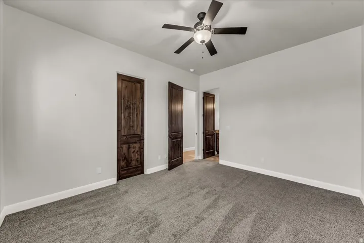Neutral wall paint, textured carpeting, contemporary ceiling fan with light, and rich wood-finish doors