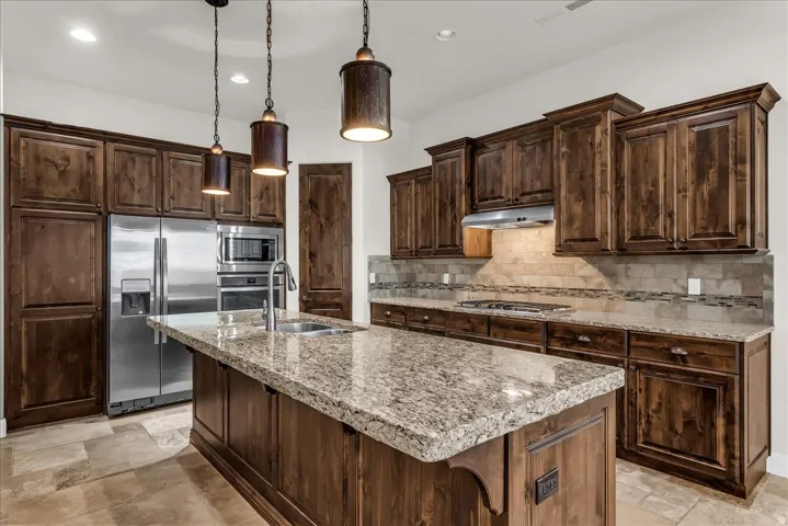 Kitchen featuring extensive dark wood cabinetry, a large central island with a stone countertop, stainless steel appliances, a tile backsplash, and coordinating tile flooring