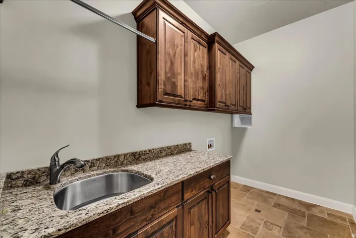 Dark wood cabinetry with crown molding, granite-style countertops, stainless steel sink with gooseneck faucet, and a built-in hanging rod