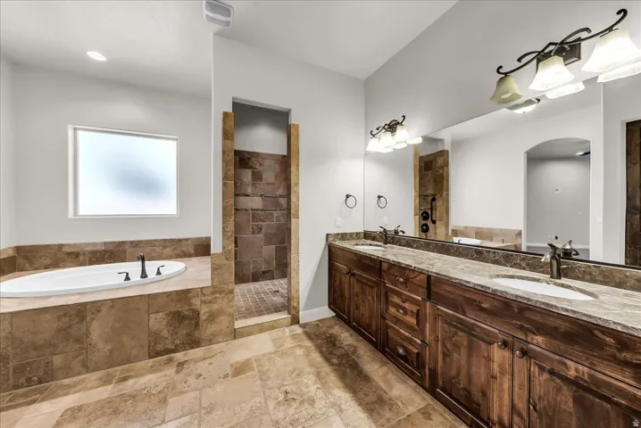 Dual vanity with undermount sinks, wood-finish cabinetry, a freestanding soaking tub, and a separate tiled shower