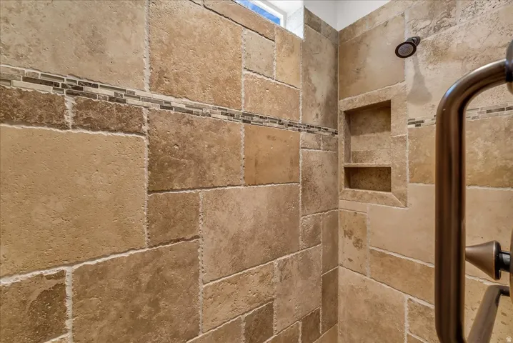 Shower stall featuring natural stone tile walls with mosaic accent, built-in shelving, a bronze showerhead, and a bronze grab bar