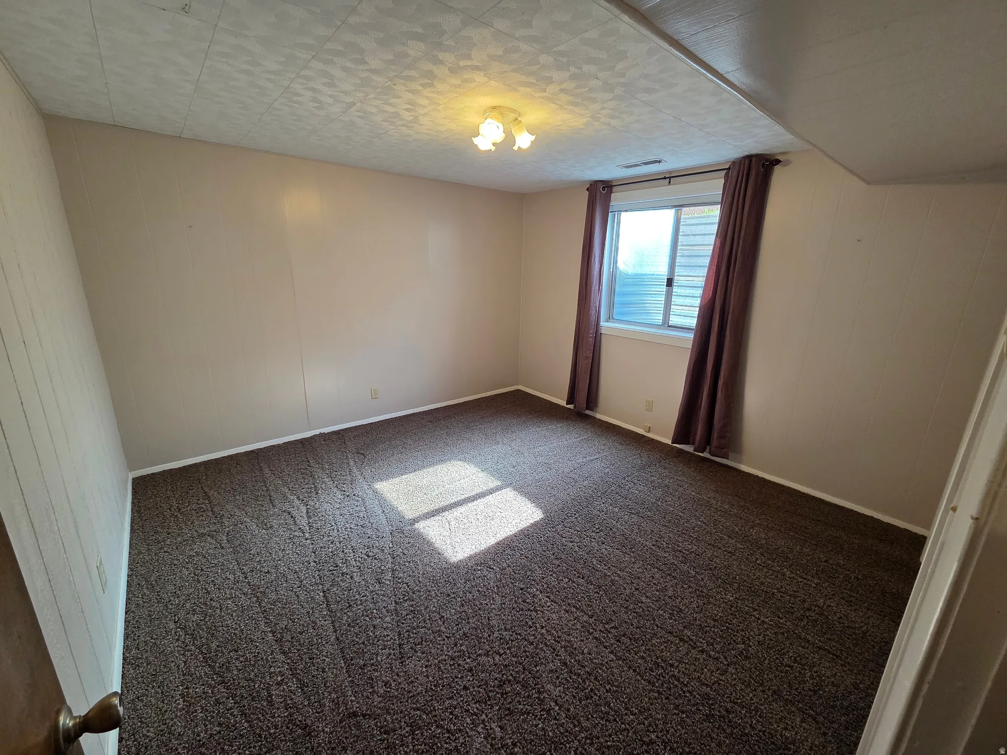 Recessed window with white frame, textured ceiling, brown carpet flooring, and a ceiling-mounted light fixture