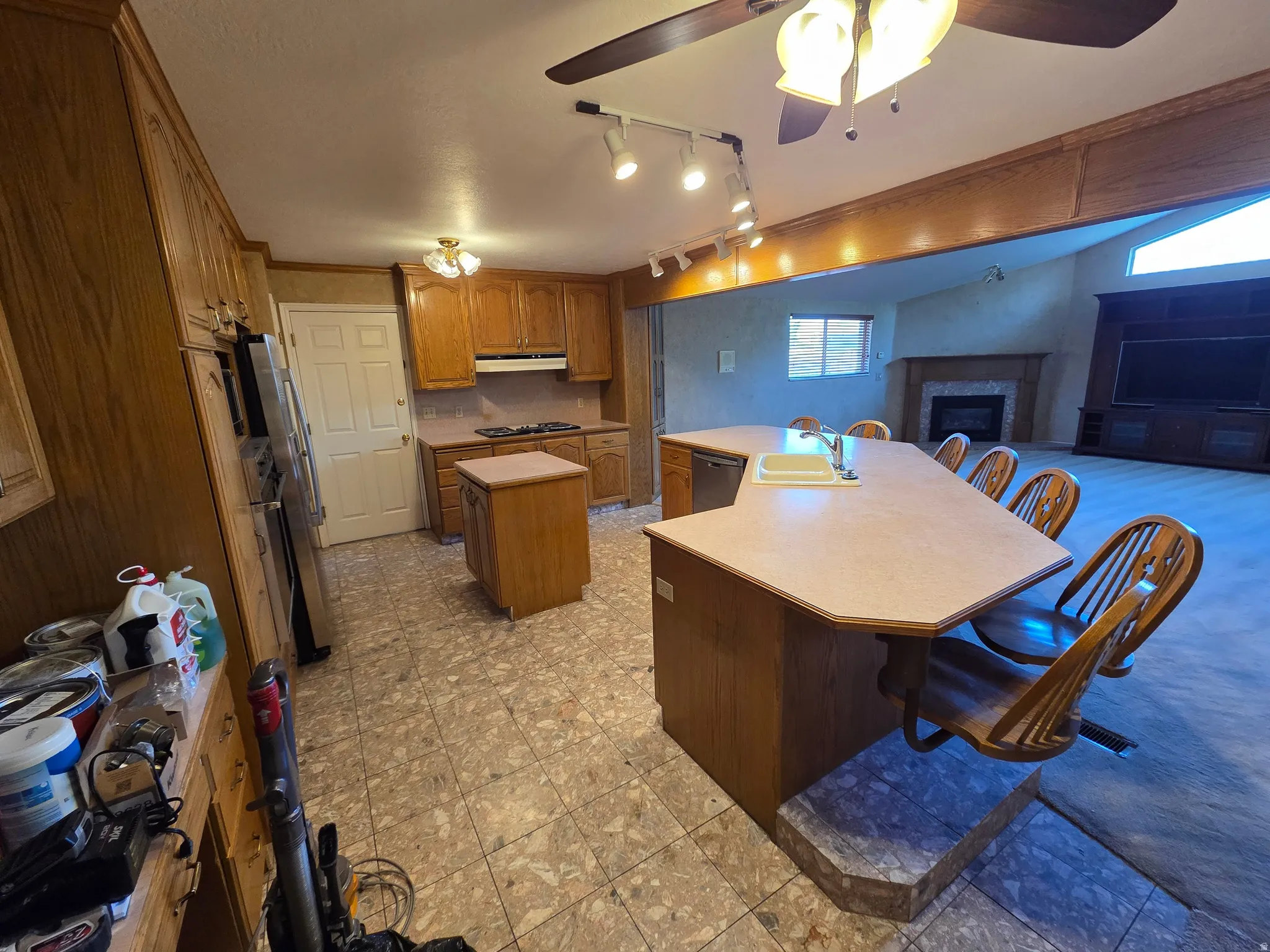 Kitchen featuring wood cabinetry, an island with integrated seating, and a built-in cooktop, opening to a living area with a fireplace