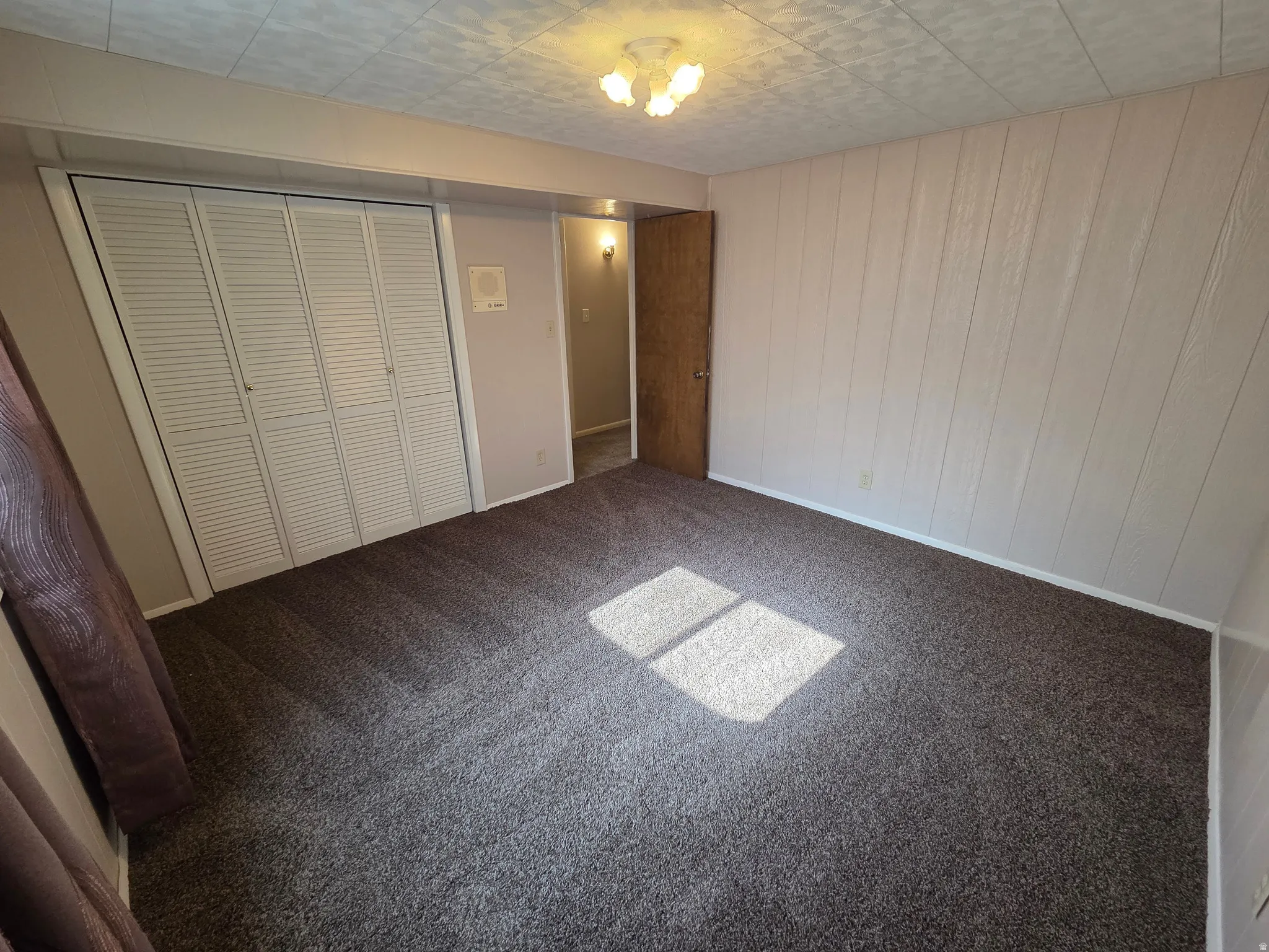 Brown textured carpet, white bi-fold closet doors, light-colored paneled walls, and a recessed ceiling light fixture