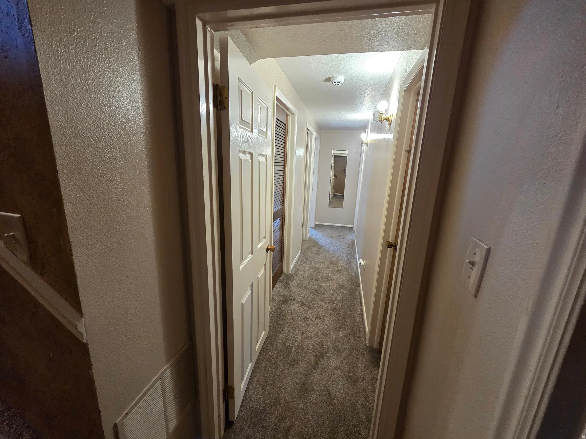Hallway with paneled doors, carpeted flooring, and wall-mounted light fixtures
