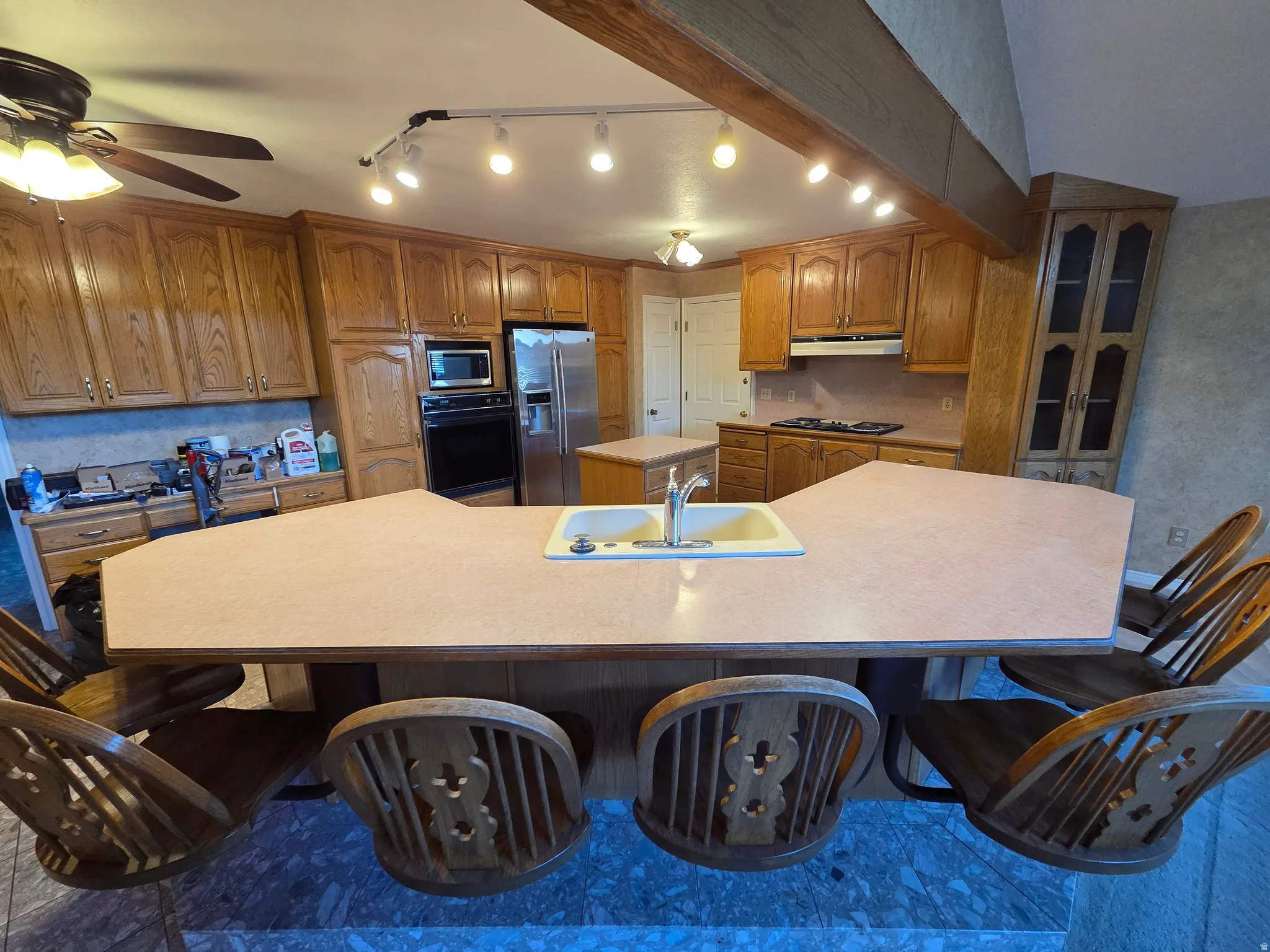 Kitchen featuring an integrated breakfast bar, wood cabinetry, a built-in oven, a stainless steel refrigerator, and track lighting