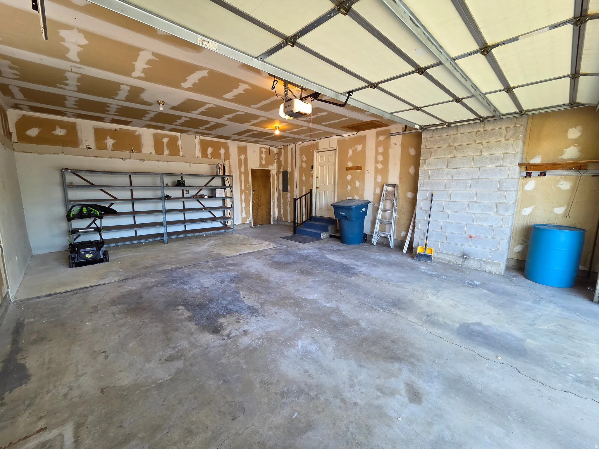 Concrete flooring, overhead garage door, built-in shelving, interior door access, and exposed ceiling joists