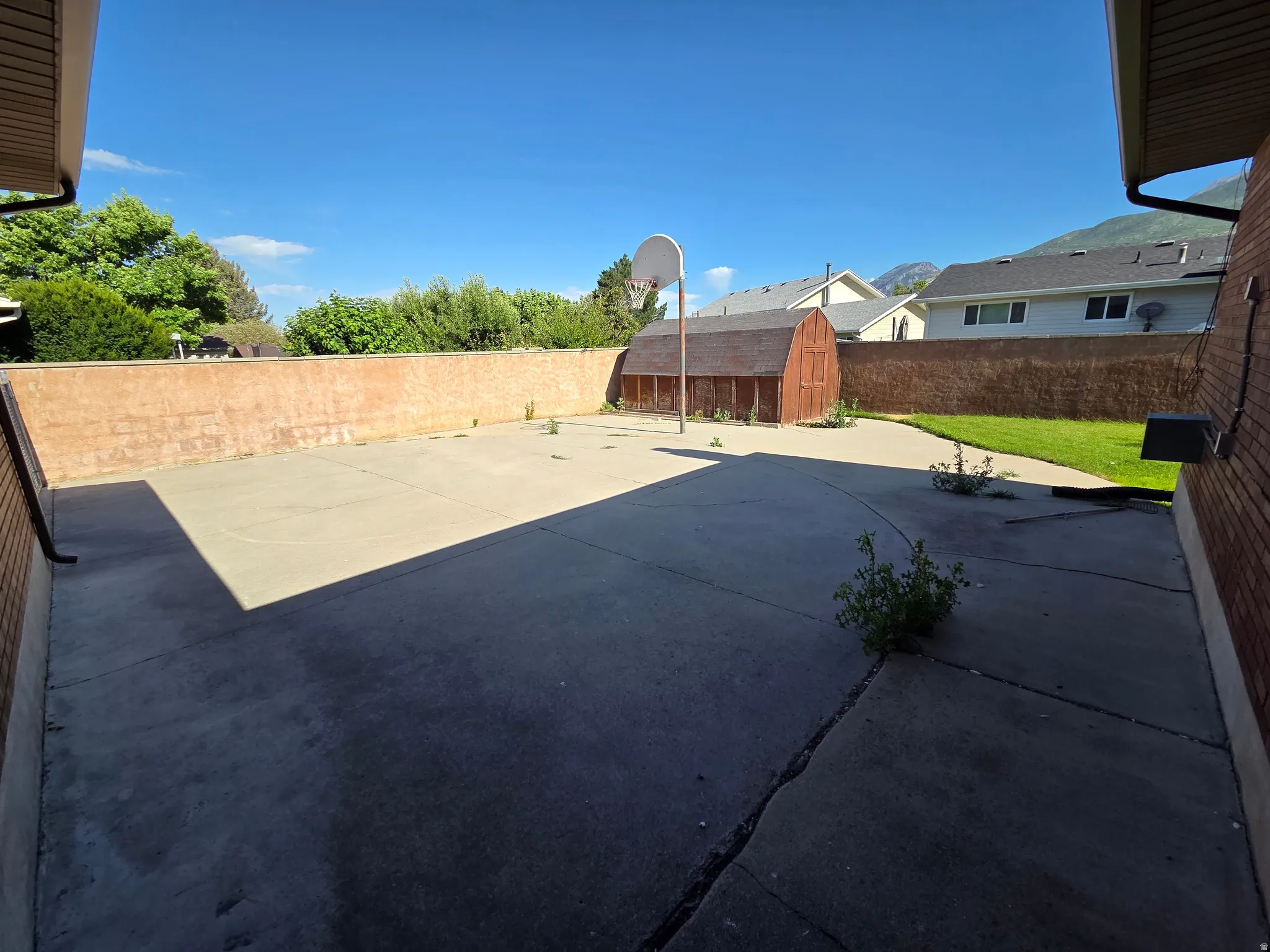 Expansive concrete patio with a basketball hoop, a detached storage shed, and a brick privacy wall