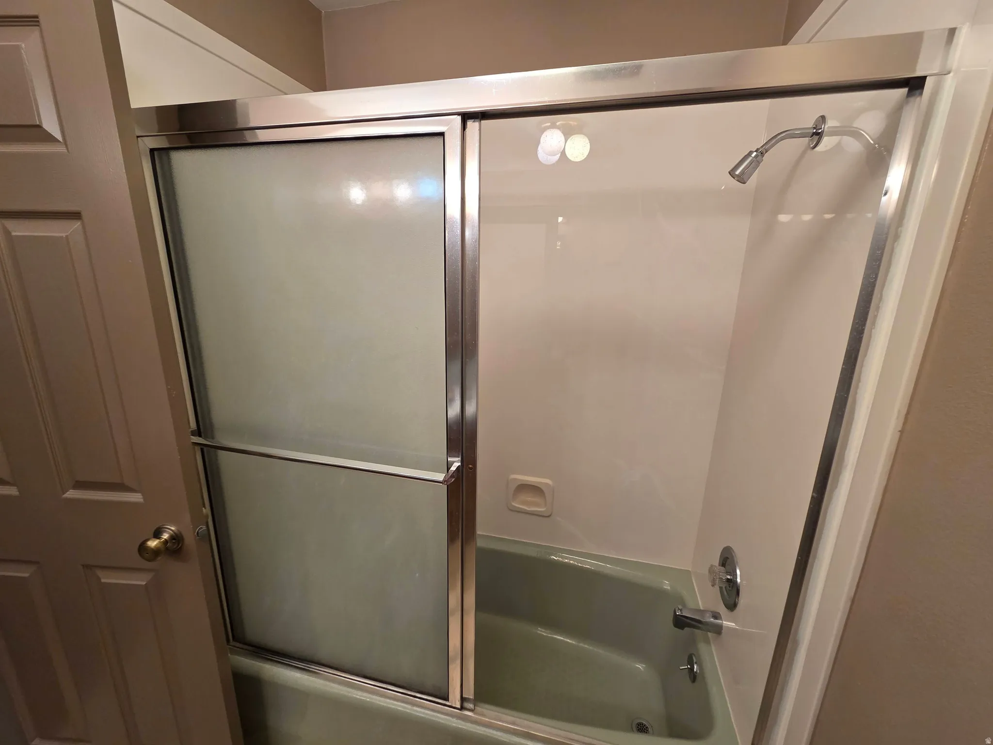 Bathtub with a shower head, polished chrome fixtures, and a sliding glass enclosure