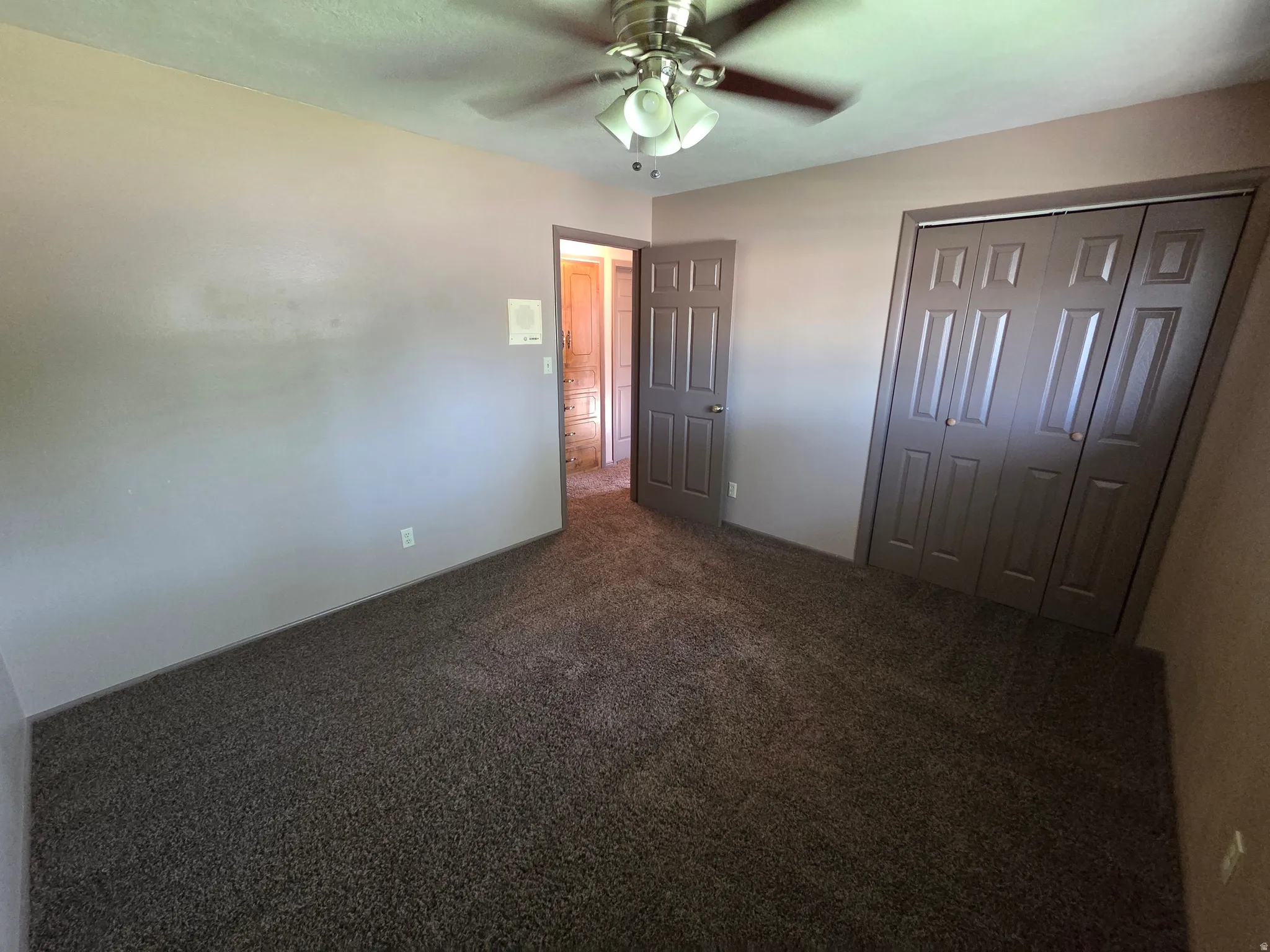 Carpeted flooring, ceiling fan with integrated lighting, wall-mounted light fixture, paneled doors, and bi-fold closet doors
