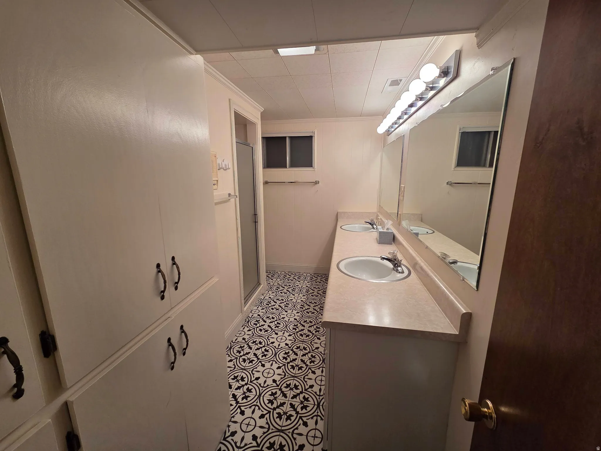 Dual vanity with integral sinks, patterned floor tile, built-in storage cabinetry, and a walk-in shower