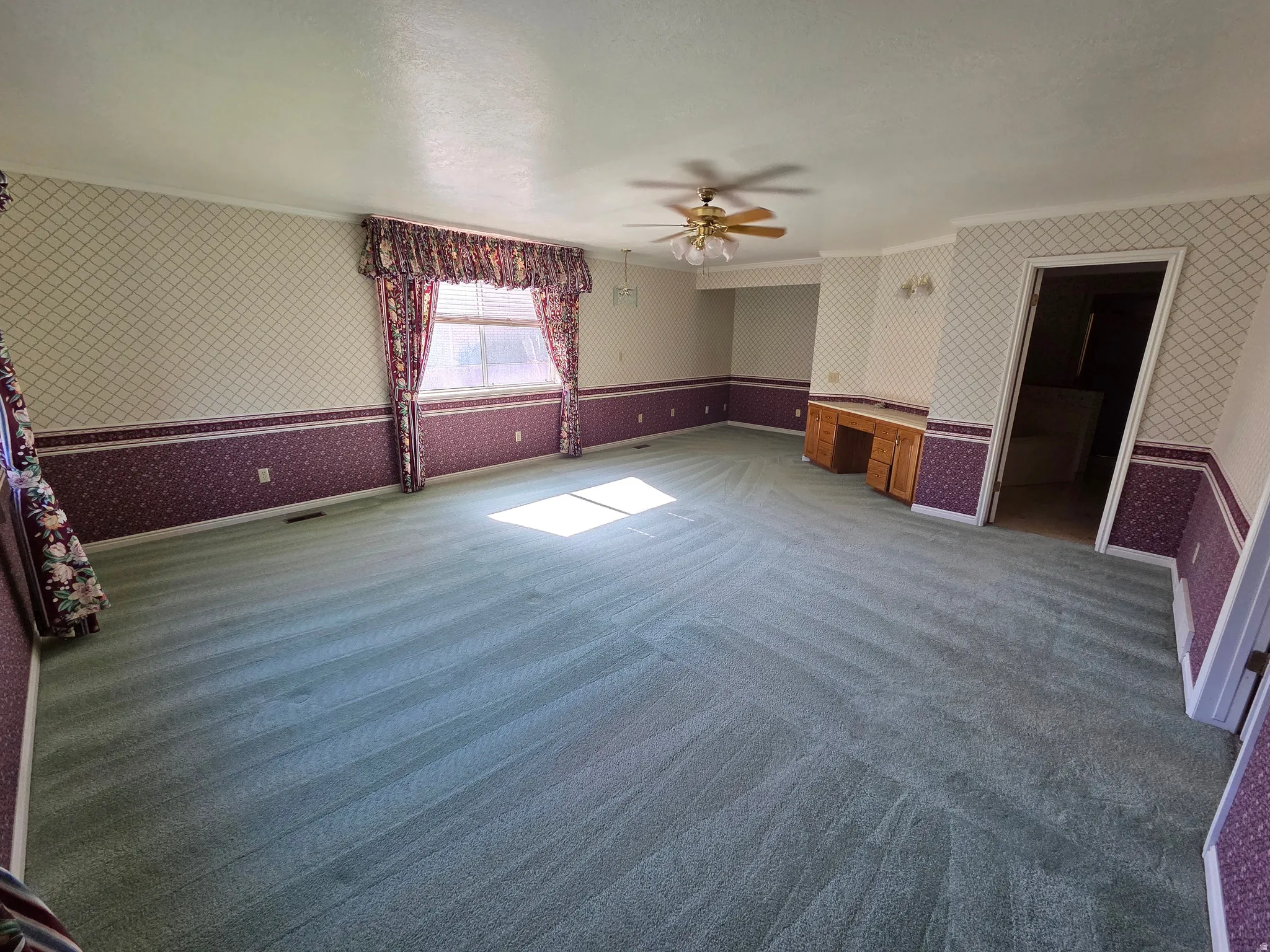Master Bedroom. Spacious room featuring patterned wallpaper, a window with valance and drapes, and a ceiling fan