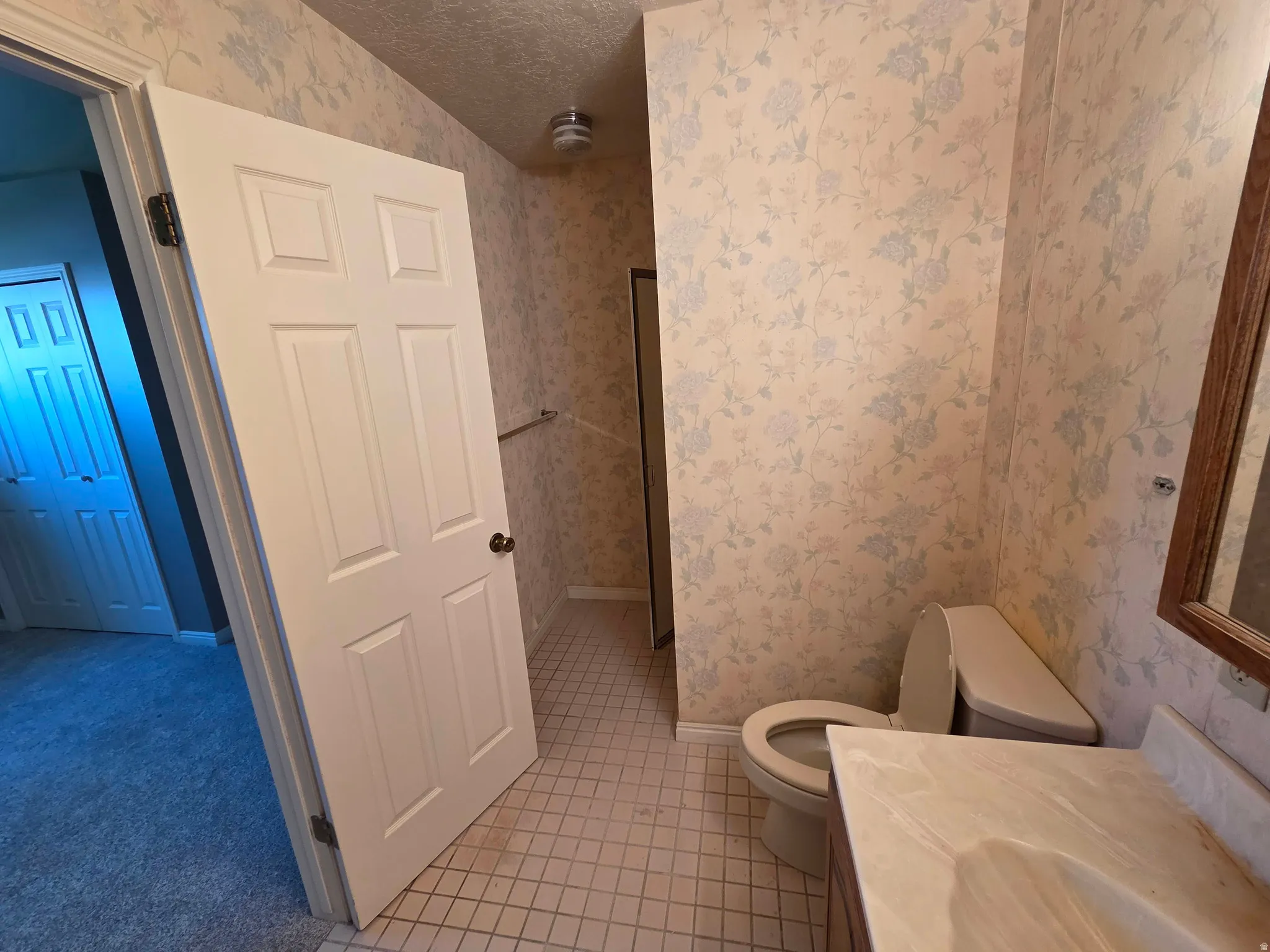 Bathroom featuring a single vanity with an integrated sink, patterned wallpaper, and tile flooring