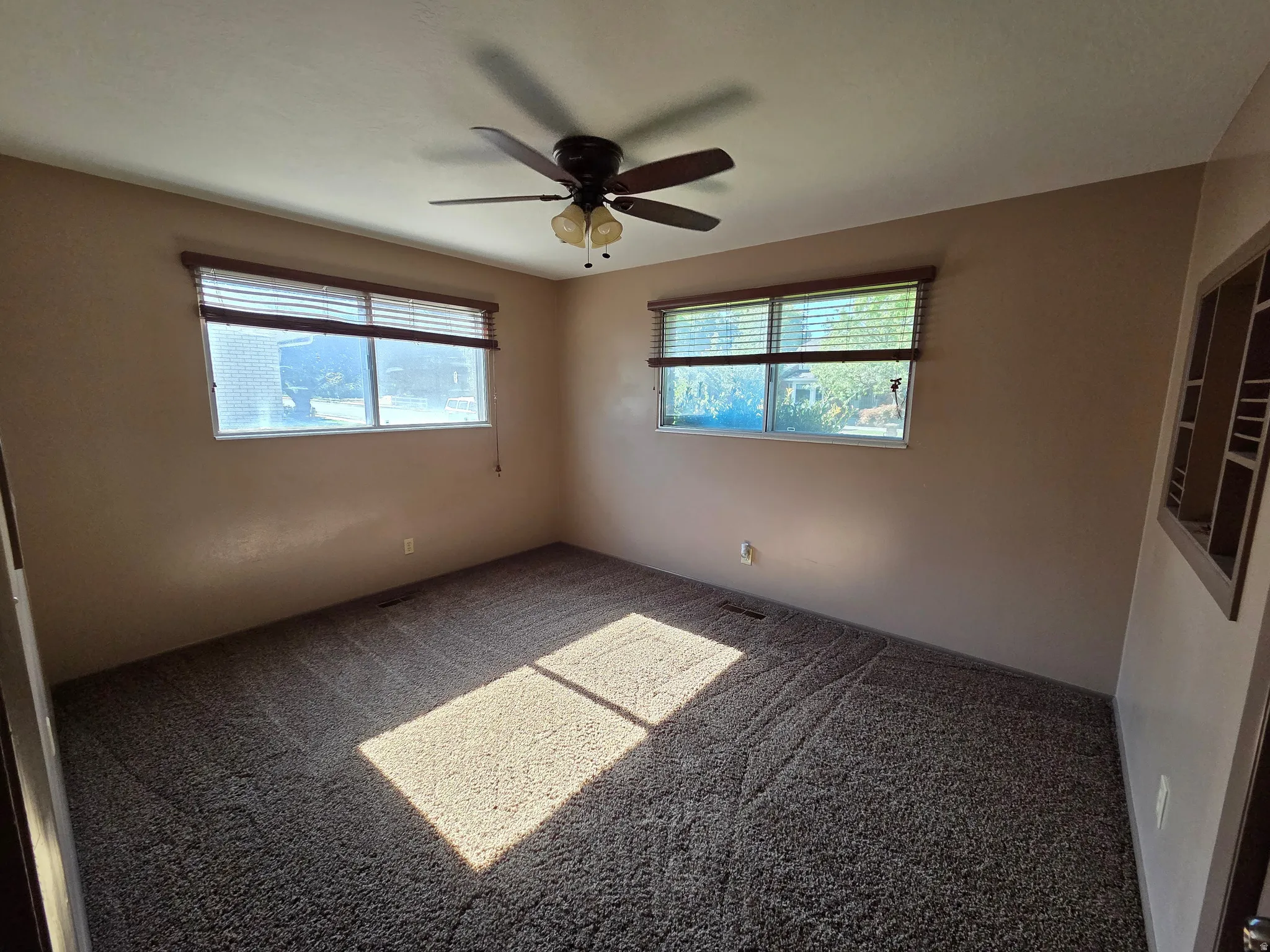 Carpeted room with two windows, a ceiling fan, and built-in shelving
