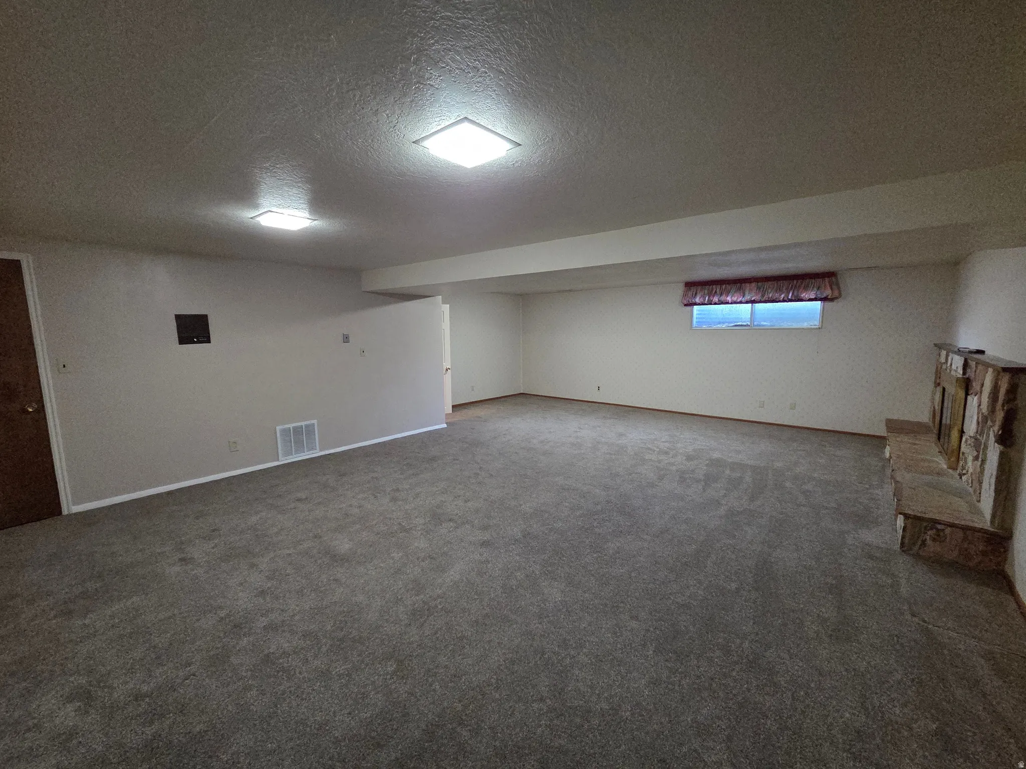 Expansive carpeted area with recessed lighting, a built-in stone fireplace, a window, and a partial wall feature