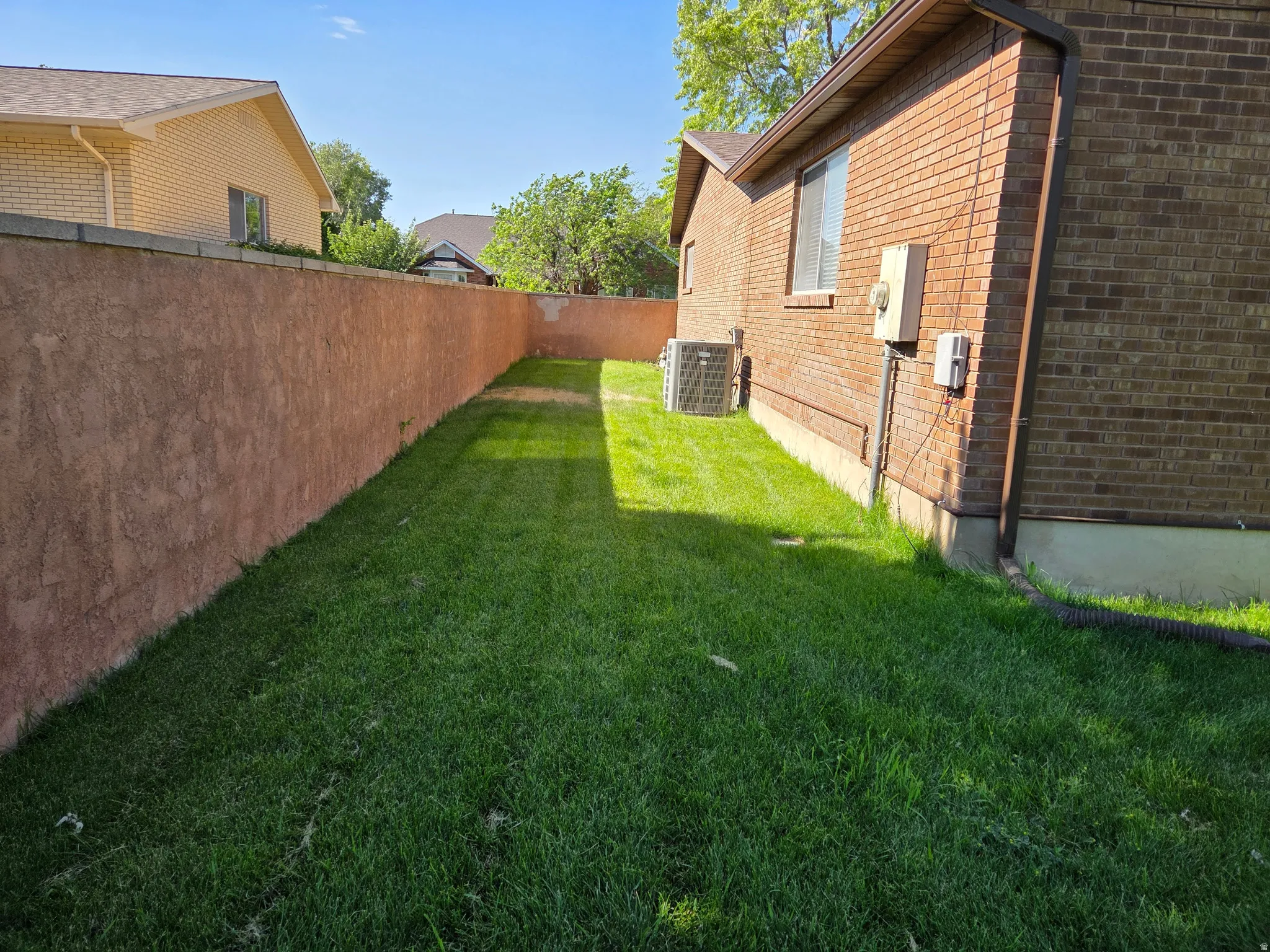 Brick exterior wall with a stucco privacy wall, lush green lawn, and visible air conditioning unit