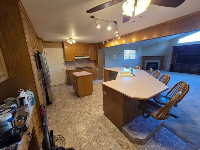 Kitchen featuring wood cabinetry, an island with integrated seating, and a built-in cooktop, opening to a living area with a fireplace