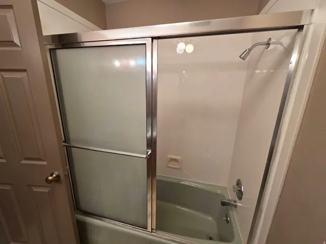 Bathtub with a shower head, polished chrome fixtures, and a sliding glass enclosure