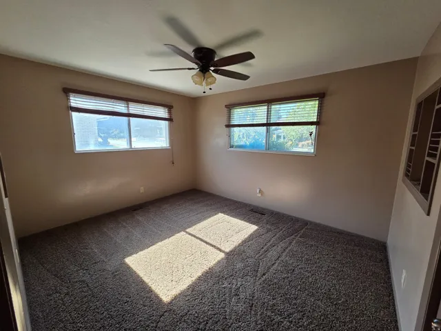 Carpeted room with two windows, a ceiling fan, and built-in shelving