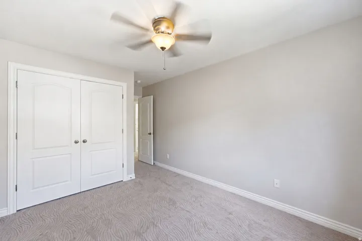 Neutral wall tones, patterned carpet, white bi-fold closet doors, and an overhead ceiling fan with integrated lighting