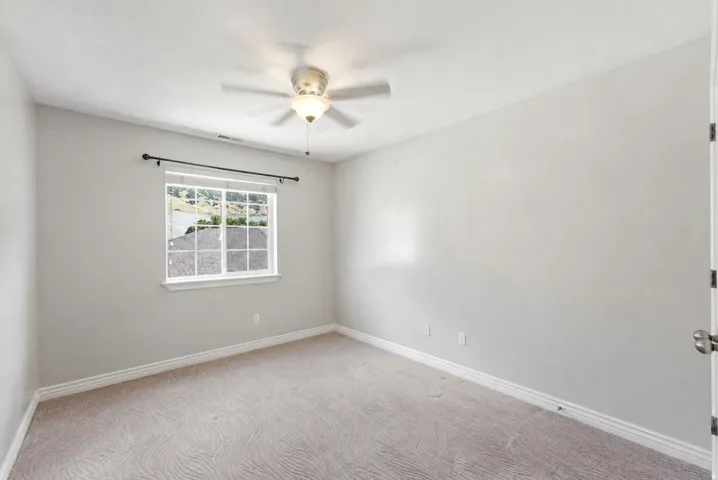 Neutral-toned walls, patterned carpeting, and a ceiling fan with integrated lighting
