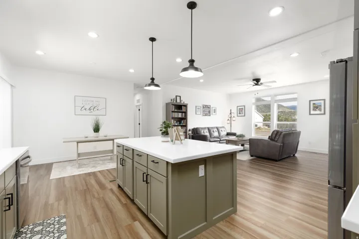 Kitchen island with white countertop and green cabinetry, wood-finish flooring, recessed lighting, and large windows