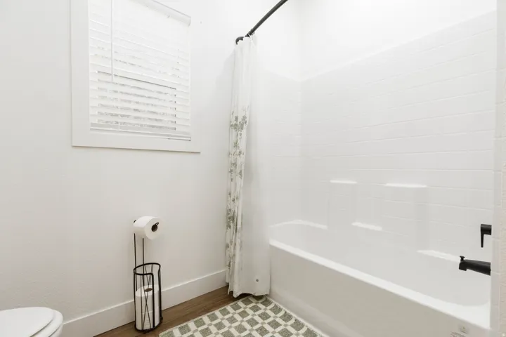 White bathtub with matte black fixtures, white subway tile surround, and wood-finish flooring