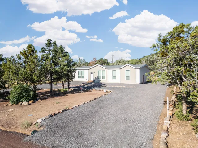 Single-story residence featuring light-colored siding, a dark roof, and a gravel driveway