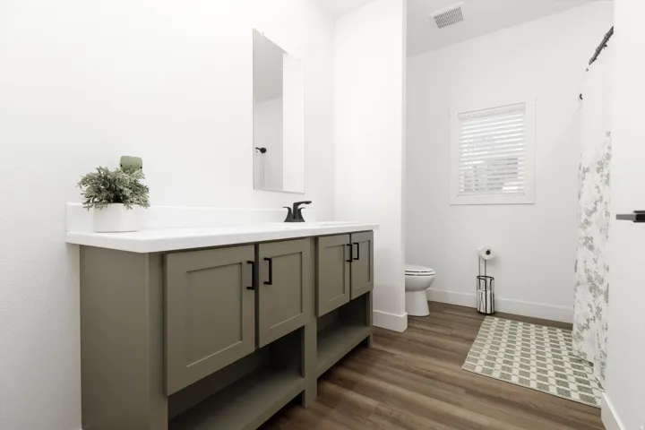 Bathroom with a gray vanity, white countertop, rectangular mirror, and wood-finish flooring