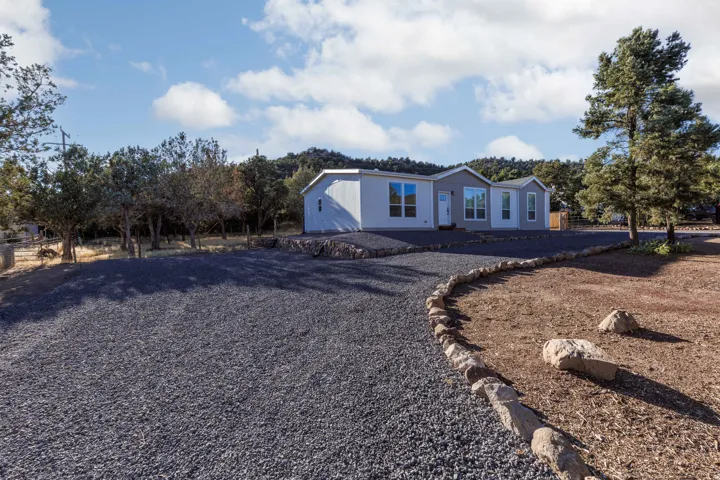 Gravel driveway with stone border, mature trees, and a light-colored exterior residence