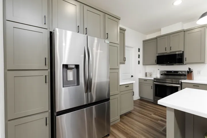 Contemporary kitchen featuring gray shaker-style cabinetry, stainless steel appliances, white countertops, and wood-finish flooring