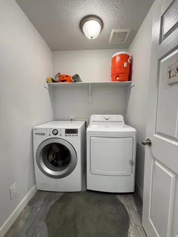 Utility room with wood-finish flooring, overhead ceiling light fixture, and wall-mounted shelving