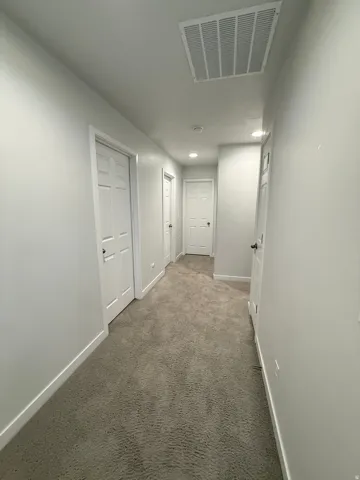 Neutral-toned carpeting, recessed ceiling lighting, white walls, white trim, and interior doors with dark hardware