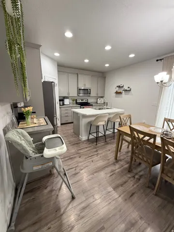 Recessed lighting, wood-finish flooring, light grey cabinetry, stainless steel appliances, and a kitchen island with seating