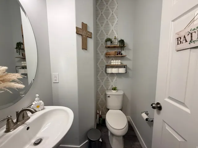 Pedestal sink with brushed nickel faucet, oval frameless mirror, and geometric pattern accent wall