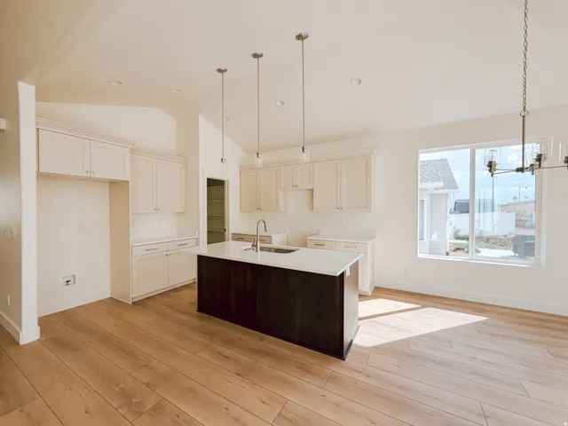 Open-concept kitchen featuring wood-finish flooring, a central island with an integrated sink, white cabinetry, and recessed lighting