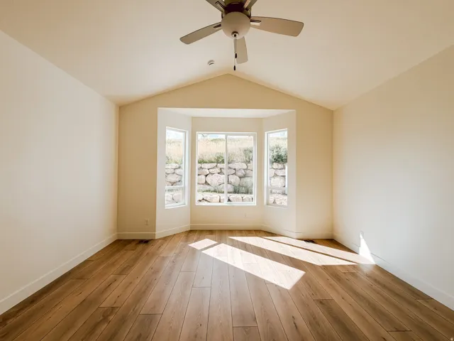 Vaulted ceiling with a ceiling fan, wood-finish flooring, and a bay window featuring three large panes