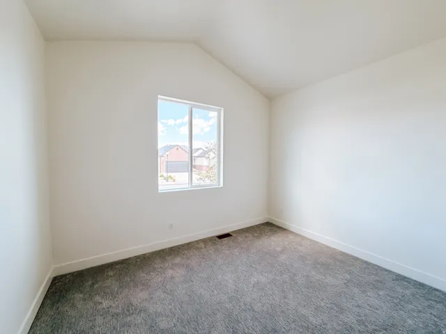 Vaulted ceiling with a single window, white walls, and gray carpeting