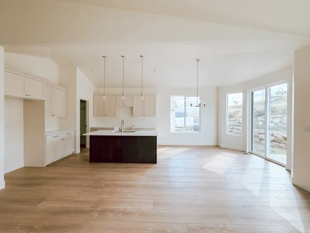 Open-concept layout with wood-finish flooring, white cabinetry, dark kitchen island with sink, and sliding glass doors