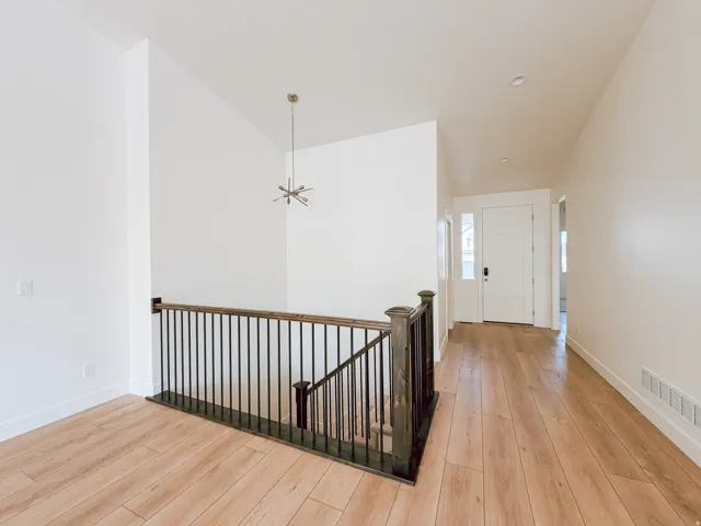 Light wood-finish flooring, white walls, black metal staircase railing with wood-finish top rail, modern chandelier, and recessed lighting