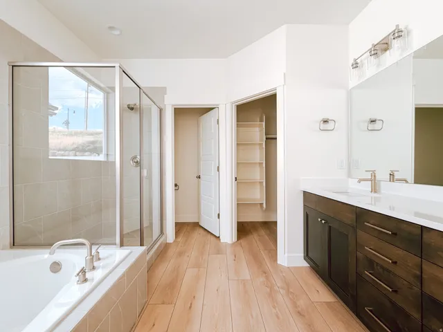 Wood-finish flooring throughout, deep soaking tub, glass-enclosed shower, dual vanity with wood cabinetry, and a walk-in closet with shelving