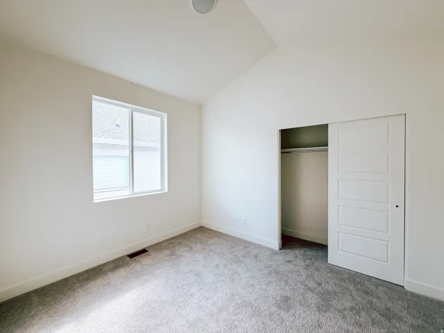 White walls with a vaulted ceiling, gray carpet, and a large window