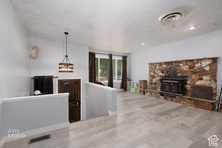 Expansive living area featuring plank-style flooring, a stone fireplace with hearth, recessed lighting, and a prominent window