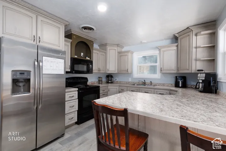 Kitchen featuring light-toned cabinetry, stainless steel refrigerator, black range, integrated microwave, and a counter-height breakfast bar