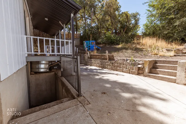 Covered exterior porch with white railing, concrete basement access, and a concrete pathway
