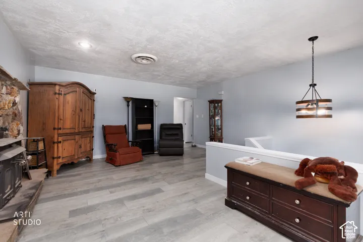 Wood-finish flooring, recessed ceiling lighting, stone fireplace surround, and a decorative hanging light fixture